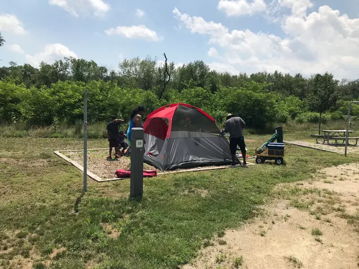 A tent pitched in a grassy field, with people nearby.
