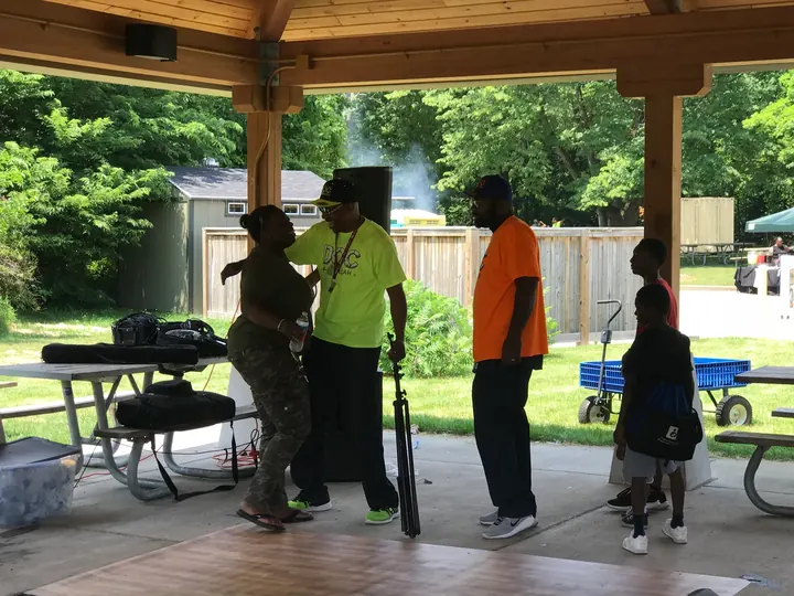 People gathered under the picnic shelter by a speaker.