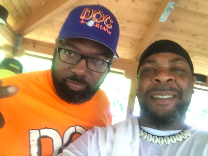 Two men smiling for a selfie under the shelter.