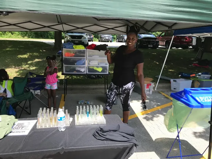 A woman standing at a vendor table of bottles under a tent.