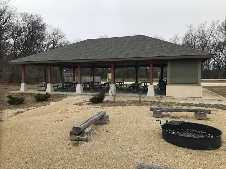A picnic shelter with a fire ring in front of it.