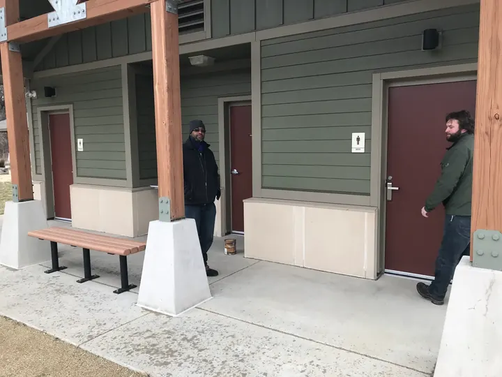 A man outside the restroom building, by a bench under the covered walkway.