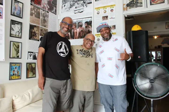 The museum's three founders standing in front of a wall of framed photos.