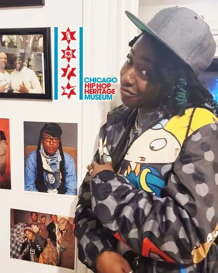 A visitor in a cap and patterned jacket posing by the photo wall.