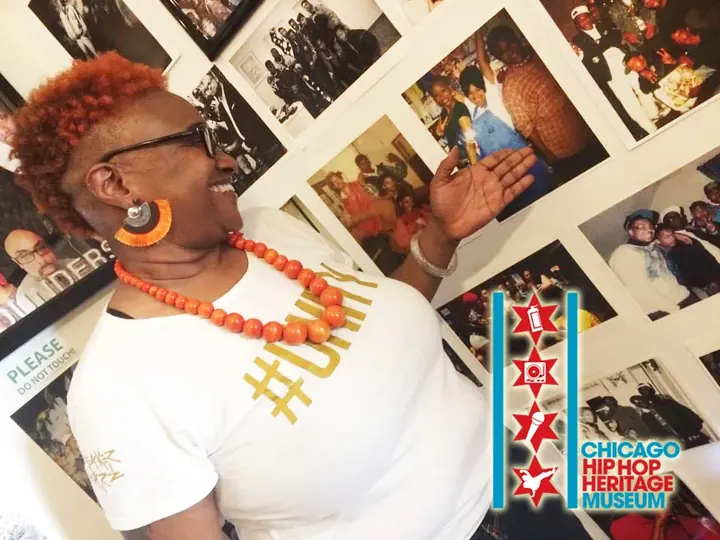 A woman in an orange necklace pointing out photos on the wall.