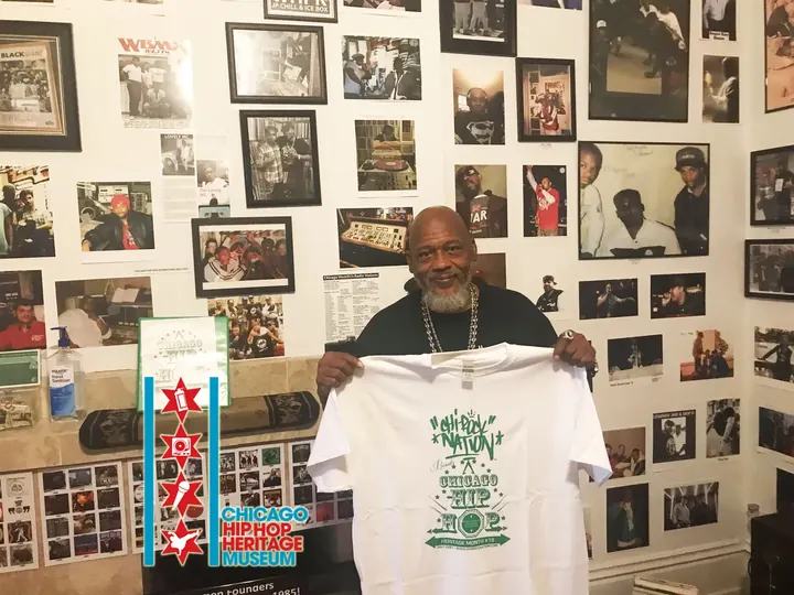 A man holding up a white T-shirt in front of the photo wall.