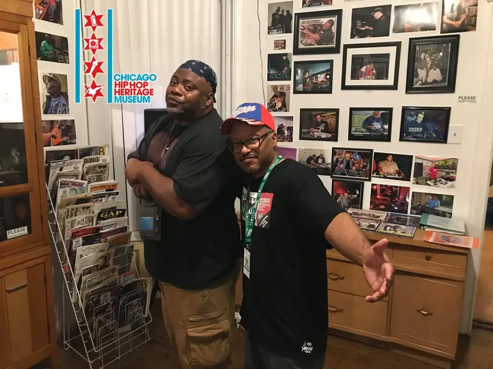 Two men posing together beside a rack of posters.